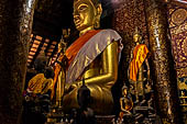 Wat Xieng Thong temple in Luang Prabang, Laos.  The main Buddha of the sim sits on a platform, surrounded by smaller statues, candles, and offerings. 